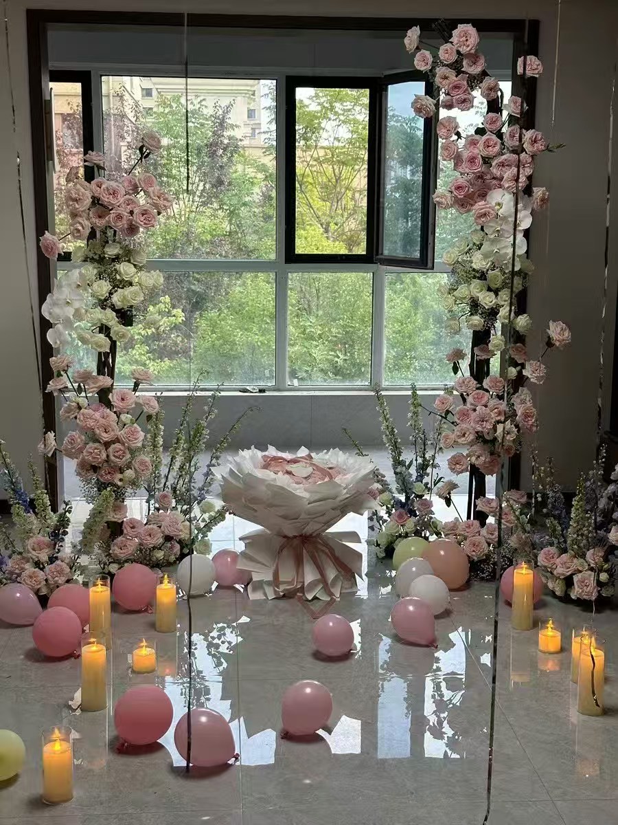Warm LED pillar candles on the floor beside pink balloons and a floral celebration display
